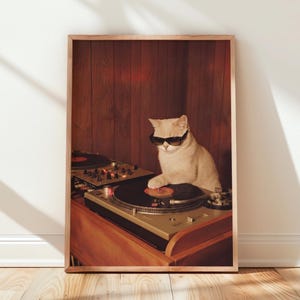 Könnte beinhalten: Ein gerahmter Wandkunstdruck, der eine helle Katze mit schwarzer Sonnenbrille zeigt, die an einem DJ-Plattenspieler mit Mischpult steht. Die Szene ist vor einem Hintergrund aus dunklen Holzpaneelen dargestellt, wobei die Katze eine Pfote auf einer Schallplatte hat.