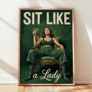 Peut inclure: Une affiche encadrée représentant une personne en tenue verte assise dans un fauteuil vert, tenant un verre à martini. Le texte en haut indique SIT LIKE et le texte en bas indique a Lady dans une police manuscrite couleur crème.