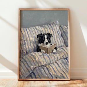 Puede incluir: Una impresión de pintura al óleo enmarcada que muestra a un perro Border Collie blanco y negro sentado erguido sobre una cama con ropa de cama a rayas azules y blancas, sosteniendo un libro abierto con sus patas. El perro mira concentrado.