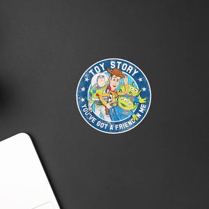 May include: A circular sticker featuring a blue background with white stars and the text TOY STORY and YOU'VE GOT A FRIEND IN ME. The center displays colorful illustrations of Woody, Buzz Lightyear, and two green aliens from the Toy Story franchise.