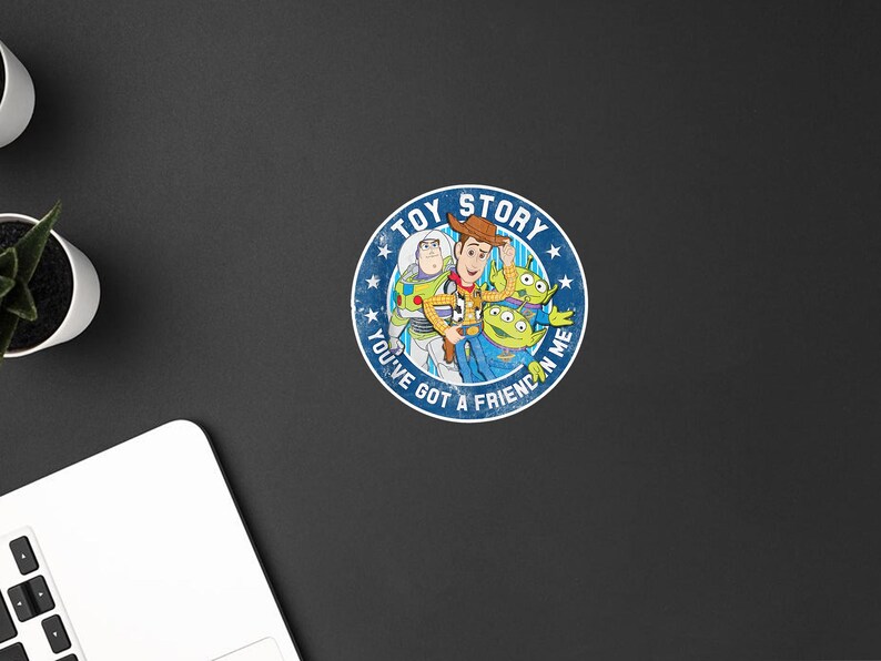 May include: A circular sticker featuring a blue background with white stars and the text TOY STORY and YOU'VE GOT A FRIEND IN ME. The center displays colorful illustrations of Woody, Buzz Lightyear, and two green aliens from the Toy Story franchise.