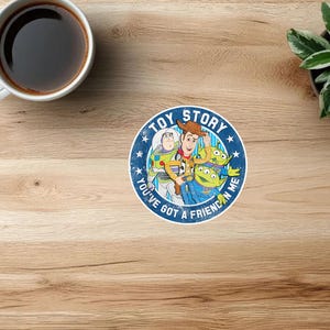 May include: A circular sticker featuring the Toy Story characters Woody, Buzz Lightyear, and two green aliens. The design includes the text TOY STORY and YOU'VE GOT A FRIEND IN ME in white lettering against a blue background with white stars.