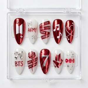 Può includere: Un set di dieci unghie finte a mandorla in una custodia di plastica trasparente. I design presentano una palette di colori rosso e bianco con finiture metalliche, tra cui il logo BTS, la parola ARMY, nomi, note musicali, una rosa e il numero 7.