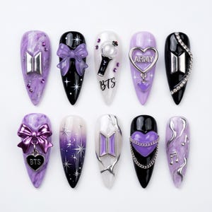 May include: Ten almond-shaped press-on nails featuring a purple and black color palette with BTS-themed designs. Embellishments include silver logos, 3D bows, heart charms, chains, rhinestones, and musical notes, with text reading BTS and ARMY.