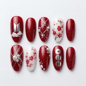Puede incluir: Un juego de diez uñas postizas con acabado de purpurina roja intensa y detalles en blanco. Los diseños incluyen un logotipo plateado, nubes blancas, líneas plateadas con perlas pequeñas, ramas florales rojas y tres círculos plateados apilados.
