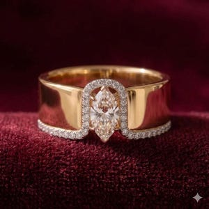 May include: A gold ring with a marquise-cut diamond center stone. The ring features a halo of smaller diamonds around the center stone and along the band. The ring is set against a deep red background.