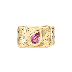 Könnte beinhalten: Ein breiter Goldring mit einem zentralen, birnenförmigen rosa Edelstein in einer Fassung. Die Oberfläche des Goldbandes hat eine unregelmäßige, texturierte Struktur und ist mit zahlreichen kleinen, runden, klaren weißen Steinen besetzt.