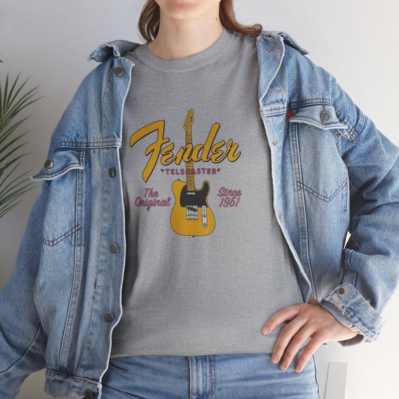 May include: A gray t-shirt featuring a Fender Telecaster guitar graphic. The design includes the Fender logo in yellow script, the word "TELECASTER", and the text "The Original Since 1951". The shirt is worn with a denim jacket.