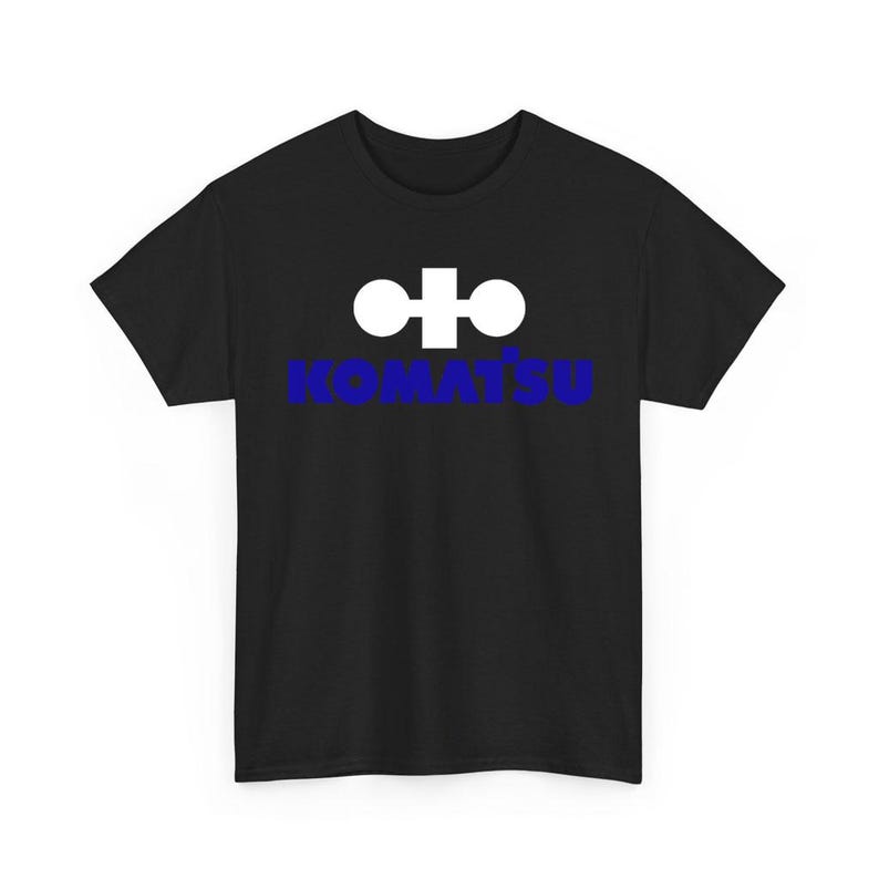 May include: A black short-sleeved t-shirt featuring a white geometric logo above the blue text KOMATSU centered on the chest. The garment has a crew neckline and a standard fit, displaying the brand name and symbol clearly against the dark fabric.