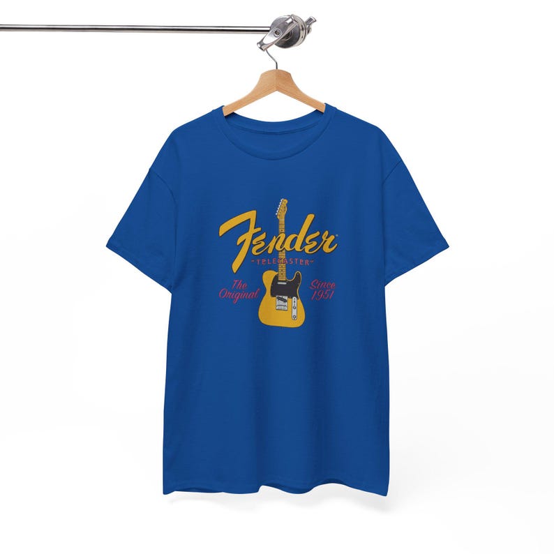 May include: A blue t-shirt featuring a yellow and black guitar graphic with the word "Fender" in yellow script. The text "TELESTER" and "The Original" are also present, along with "Since 1951".