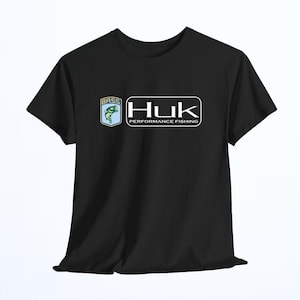 May include: A black short-sleeved t-shirt featuring a graphic on the chest. The graphic includes a blue shield with a green fish and the word BASS, next to a white rectangular logo with the text Huk PERFORMANCE FISHING in a bold font.