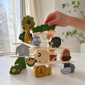 May include: A wooden balancing toy featuring various animal figures, including a giraffe, crocodile, and lion. The toy is constructed with wooden planks and colorful animal shapes, promoting fine motor skills and imaginative play.