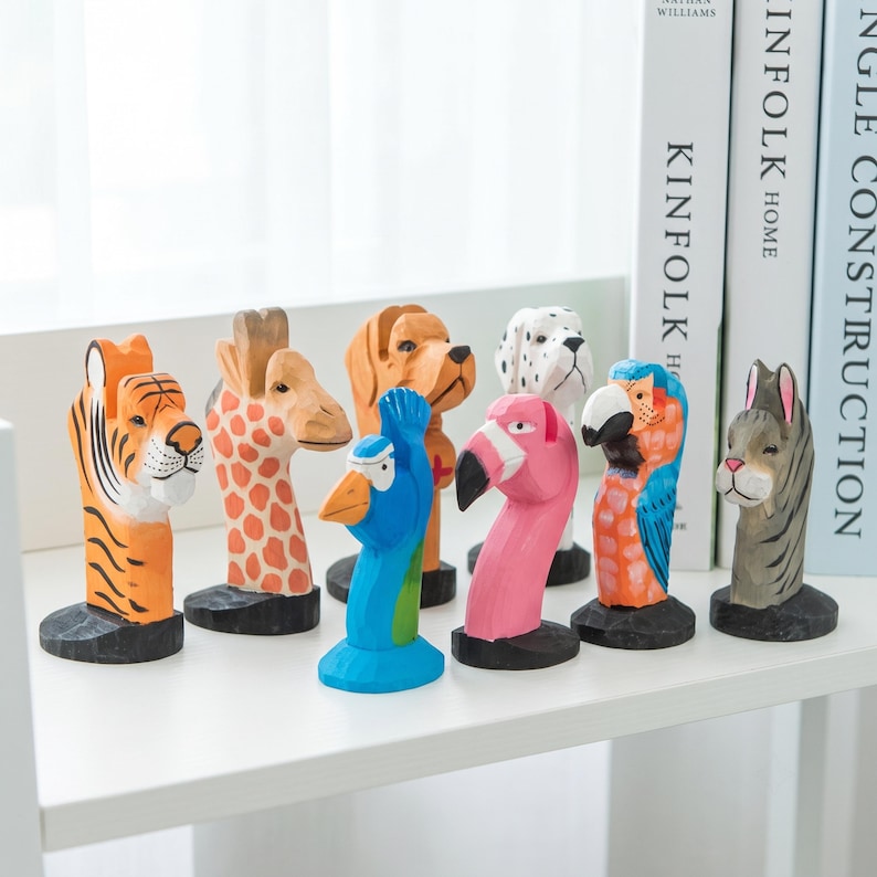 May include: A collection of eight hand-carved wooden animal figurines featuring a tiger, giraffe, dog, peacock, flamingo, parrot, and zebra. Each figure is painted in vibrant colors and stands on a small black circular base, arranged in a group.
