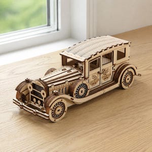 May include: A wooden model of a vintage car with intricate details. The car is light brown with visible wooden grain, featuring detailed wheels, a radiator, and the text "CLASSIC" on the front. The model is on a light brown surface.