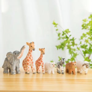 May include: A collection of wooden animal figurines, including an elephant, two giraffes, a polar bear, a zebra, a bear, and a sheep. The elephant is gray, the giraffes have orange and brown spots, and the other animals are white and brown.