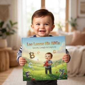 May include: A child smiles while holding a book titled "Leo Learns His ABCs." The book cover shows a child holding a red letter A in a field with letters and a zebra. The book's subtitle reads "Learn, Laugh & Explore."