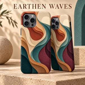 May include: Two smartphone cases featuring a layered, abstract wave pattern in shades of terracotta, teal, cream, and deep burgundy. The text EARTHEN WAVES is printed above the cases. Each case has a cutout for a triple-lens camera system.