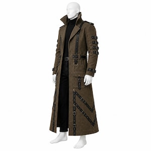 May include: A long brown coat featuring black leather-like straps, multiple silver-toned buckles on the sleeves and front panels, a high collar, and large flap pockets. The coat is worn over a black turtleneck sweater and black trousers.