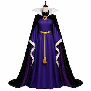 May include: A floor-length purple gown with long, wide sleeves featuring white cuffs. The dress includes a black velvet cape with a high white collar, a gold-toned belt with a long tassel, and a decorative brooch with a large red stone at the neck.