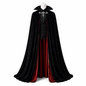 May include: A floor-length black velvet cape with a deep red lining, featuring a high collar and a silver-toned ornate metal clasp at the neck. The cape is displayed over a black button-down shirt and a black vest on a white mannequin torso.