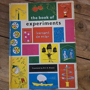 May include: A vintage book titled "The Book of Experiments" with colorful illustrations. The cover features a variety of images, including a beaker, a cartoon character, and a boat. The author's name, Leonard de Vries, is also visible.