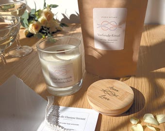 May include: A white candle in a glass jar, a brown paper pouch labelled Vorfreude-Ritual, a wooden lid engraved with the names Anna and Lena, and a white card with German text asking a question, accompanied by scattered white flower petals.