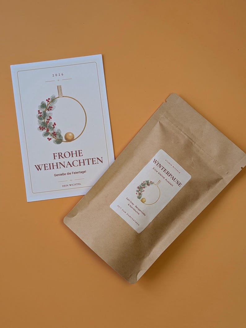 May include: A rectangular white card with the text FROHE WEIHNACHTEN and a wreath illustration, alongside a brown paper pouch labelled WINTERPAUSE with a matching wreath graphic, Earl Grey, Bergamotte, and Kornblume text, and a small gold ball.