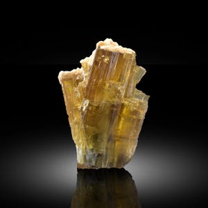 Könnte beinhalten: Ein rohes, durchscheinendes goldgelbes Mineralexemplar, bestehend aus einer Ansammlung vertikal gestreifter, prismatischer Kristalle. Die Struktur zeigt verschiedene Bernstein- und Honigtöne mit einer gezackten, kristallinen Oberkante und einer reflektierenden Oberfläche.