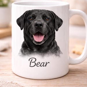 May include: A white ceramic mug featuring a high-resolution photographic print of a black Labrador retriever with its mouth open and tongue visible. Below the dog portrait, the name Bear is printed in a dark gray cursive script font.