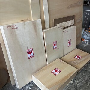 May include: Several rectangular light-colored wooden panels and boxes of varying sizes. Each piece features a white sticker with a red border and a red wine glass icon, containing the text DIKKAT KIRILIR and FRAGILE in bold black lettering.