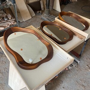 May include: Three oval-shaped mirrors with thick, dark brown wooden frames featuring irregular, organic edges. Each mirror is set within a light-colored wooden tray. The reflective surfaces show small orange square markers and a white circular knob.