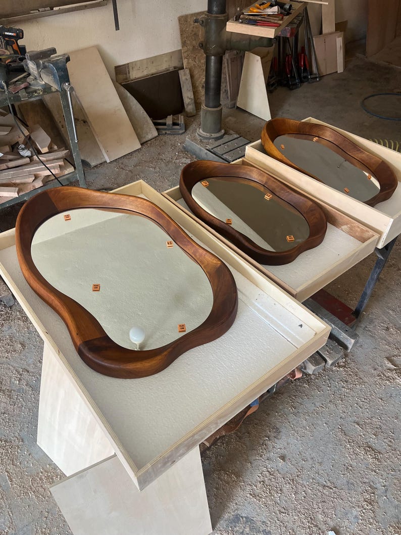 May include: Three oval-shaped mirrors with thick, dark brown wooden frames featuring irregular, organic edges. Each mirror is set within a light-colored wooden tray. The reflective surfaces show small orange square markers and a white circular knob.