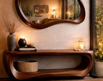 May include: A modern, dark wood console table with a matching, organically shaped mirror. The table features a lower shelf and a woven basket. Decorative items include a vase, candle, and books. The room has a neutral color palette.
