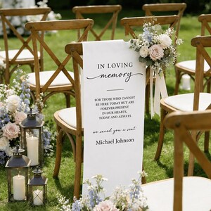 Pode incluir: Uma placa memorial de tecido branco sobre uma cadeira de madeira com encosto cruzado. O texto diz: IN LOVING memory FOR THOSE WHO CANNOT BE HERE TODAY BUT ARE FOREVER PRESENT IN OUR HEARTS, TODAY AND ALWAYS we saved you a seat Michael Johnson.