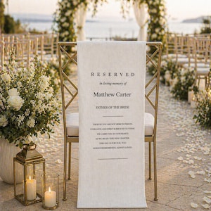 Pode incluir: Uma cadeira dourada com uma faixa de tecido branco que diz "RESERVED in loving memory of Matthew Carter FATHER OF THE BRIDE". A faixa tem um poema impresso. A cena é um casamento ao ar livre com arranjos florais e velas.