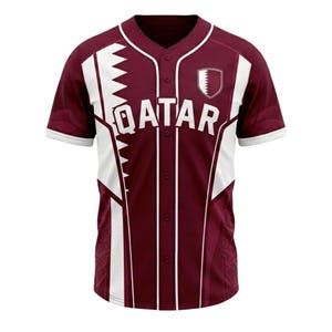 May include: Maroon baseball jersey with white detailing and the word "QATAR" across the chest. The jersey has a button-up front, short sleeves, and a shield emblem on the right chest.