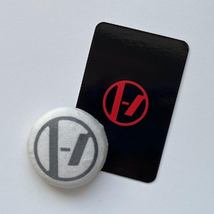 May include: A circular white button featuring a grey circular logo with a vertical line and a dash, positioned next to a rectangular black card displaying the same logo in a vibrant red colour. The design is consistent across both items.