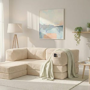 May include: A modular beige corduroy sofa with a matching ottoman, featuring a textured fabric finish. A light green knit throw blanket is draped over one armrest, and a small black remote control is tucked into the side pocket of the sofa.
