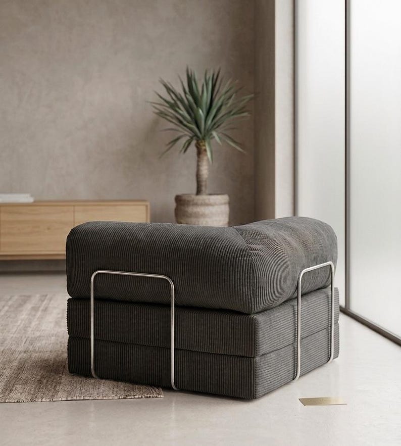 May include: A low-profile, square-shaped modular chair upholstered in dark gray corduroy fabric. The seat features a thick, cushioned design supported by a sleek, silver-toned metal frame that wraps around the sides and base of the furniture piece.