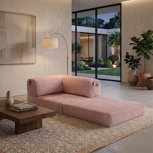 May include: A low-profile, pink corduroy modular sofa with a corner backrest and integrated side pockets. The sofa features a textured fabric finish and a rectangular shape, positioned on a woven rug in a room with a wooden coffee table and floor lamp.