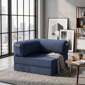 May include: A navy blue corduroy modular floor chair featuring a low-profile design with a square backrest and seat. The chair includes integrated side pockets on the armrests and is draped with a light gray textured throw blanket.