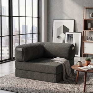 May include: A dark gray corduroy modular floor chair featuring a low-profile design with a thick seat and backrest. The chair includes integrated side pockets on the armrests and is draped with a light gray textured throw blanket.