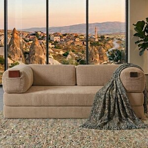 May include: A beige corduroy sofa with two rectangular cushions and integrated side pockets. A dark gray textured throw blanket with fringe is draped over the right armrest. The sofa features a ribbed fabric texture and a low-profile design.