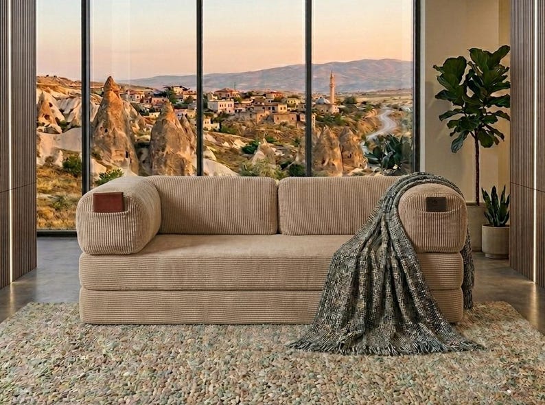May include: A beige corduroy sofa with two rectangular cushions and integrated side pockets. A dark gray textured throw blanket with fringe is draped over the right armrest. The sofa features a ribbed fabric texture and a low-profile design.