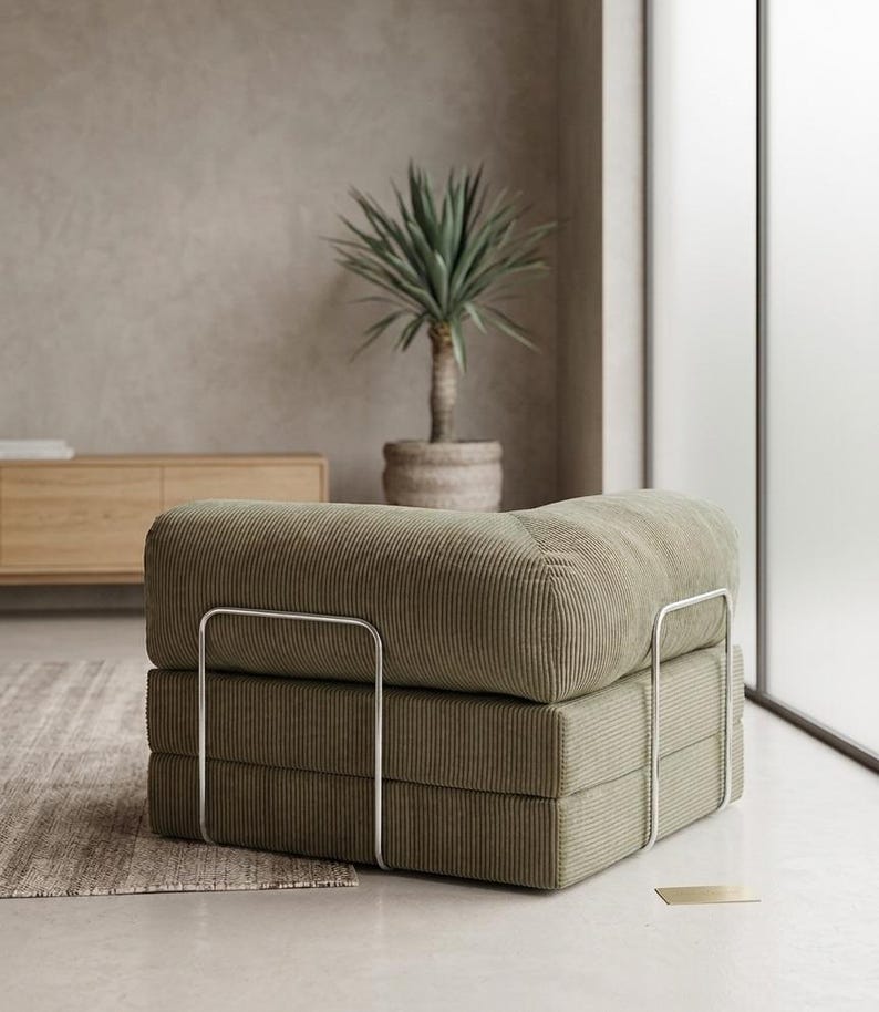 May include: A low-profile modular armchair upholstered in olive green corduroy fabric. The seat features a thick, square-shaped cushion and a backrest, supported by a sleek, silver-toned metal frame that wraps around the exterior sides.