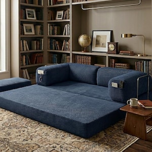May include: A navy blue corduroy floor sofa with a low-profile design, featuring two integrated side armrests with built-in storage pockets, a matching rectangular ottoman, and a wide, flat seating area upholstered in a textured fabric.