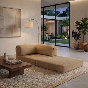 May include: A low-profile, tan corduroy modular sofa with a corner backrest and integrated side pockets, positioned on a textured rug next to a dark wood coffee table holding a small vase and stacked books, illuminated by a curved floor lamp.