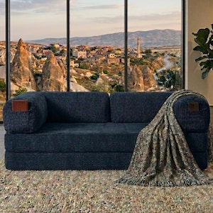 May include: A dark blue corduroy sofa with a rectangular brown leather accent on each armrest. A textured, multi-colored throw blanket with fringe edges is draped over the right side of the sofa, covering the armrest and part of the seat cushion.