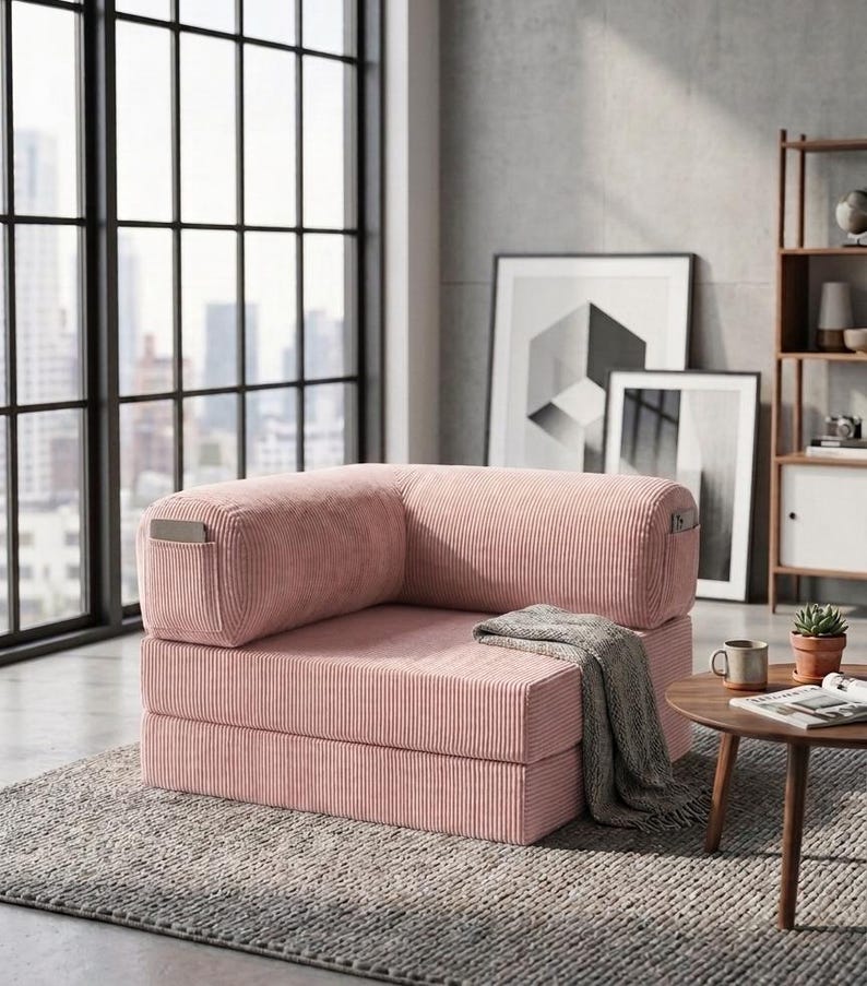 May include: A pink corduroy modular floor chair with a low-profile, rectangular design. The chair features a thick, cushioned seat and backrest with vertical ribbed texture, and includes small side pockets on the outer armrests for storage.