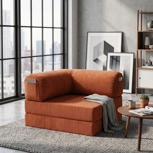 May include: A modular corner chair upholstered in burnt orange corduroy fabric. The chair features a low-profile design with a thick seat cushion, a backrest, and side armrests. A grey knit throw blanket is draped over the seat cushion.